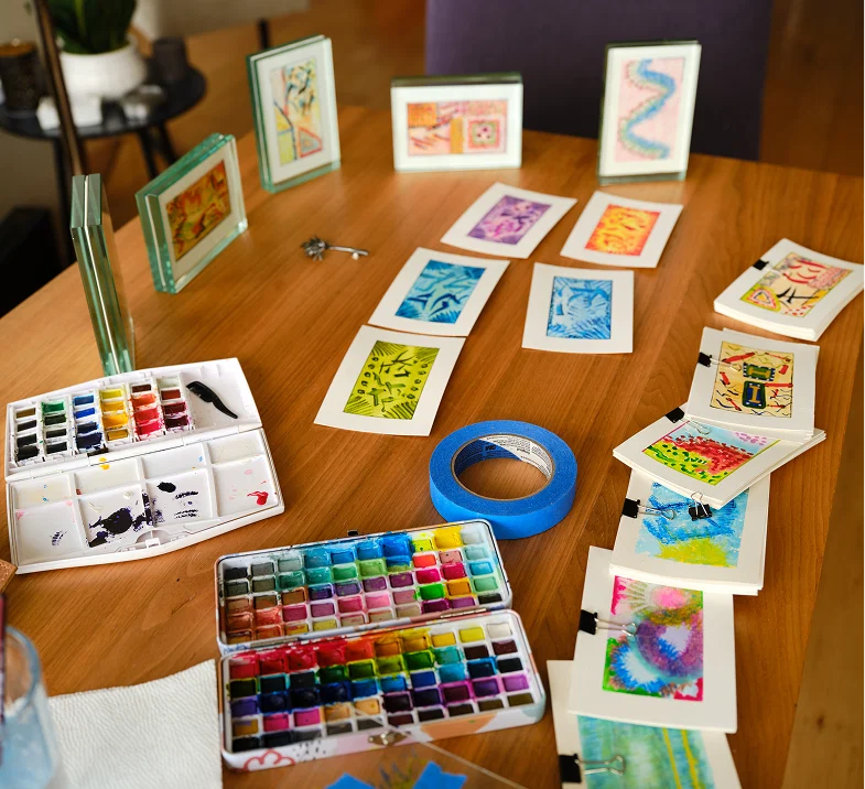 Watercolor palettes and finished postcards laid out on the table